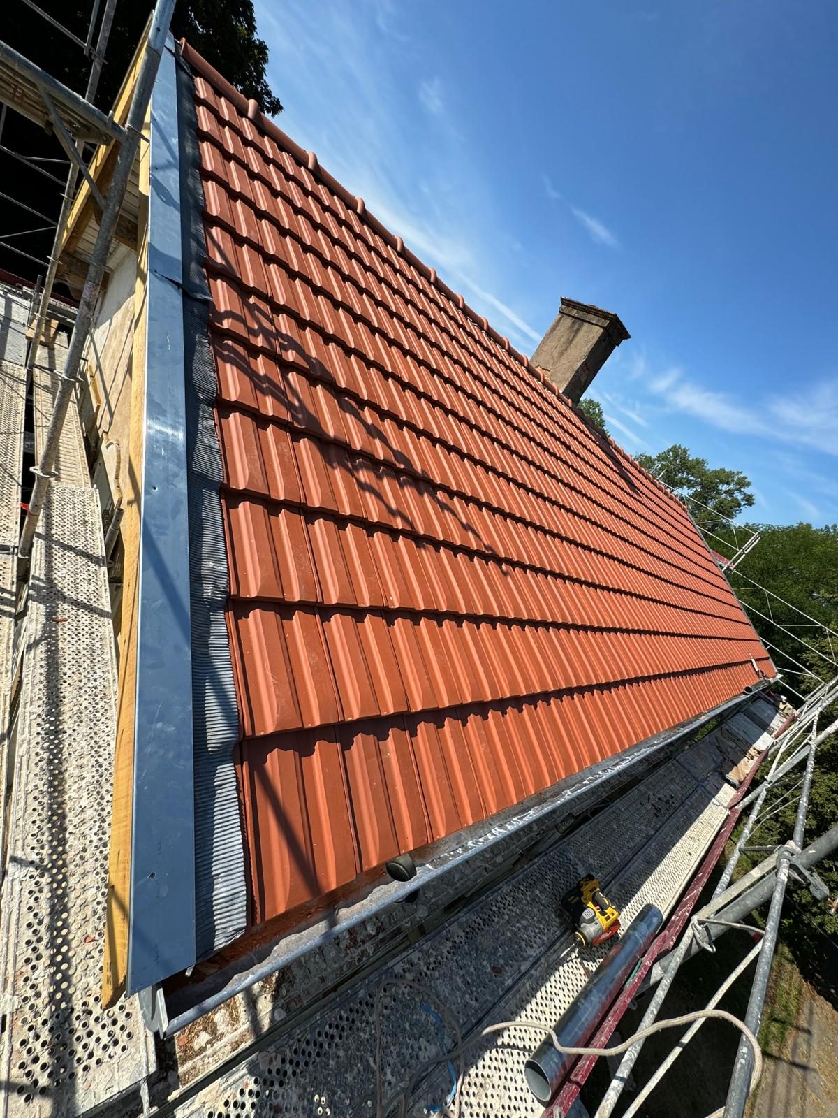 Versant de tuiles neuves, échafaudage et cheminée sous le ciel bleu